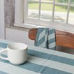 Essential Striped Tablecloth in Sky with Essential Mug on table with chair.