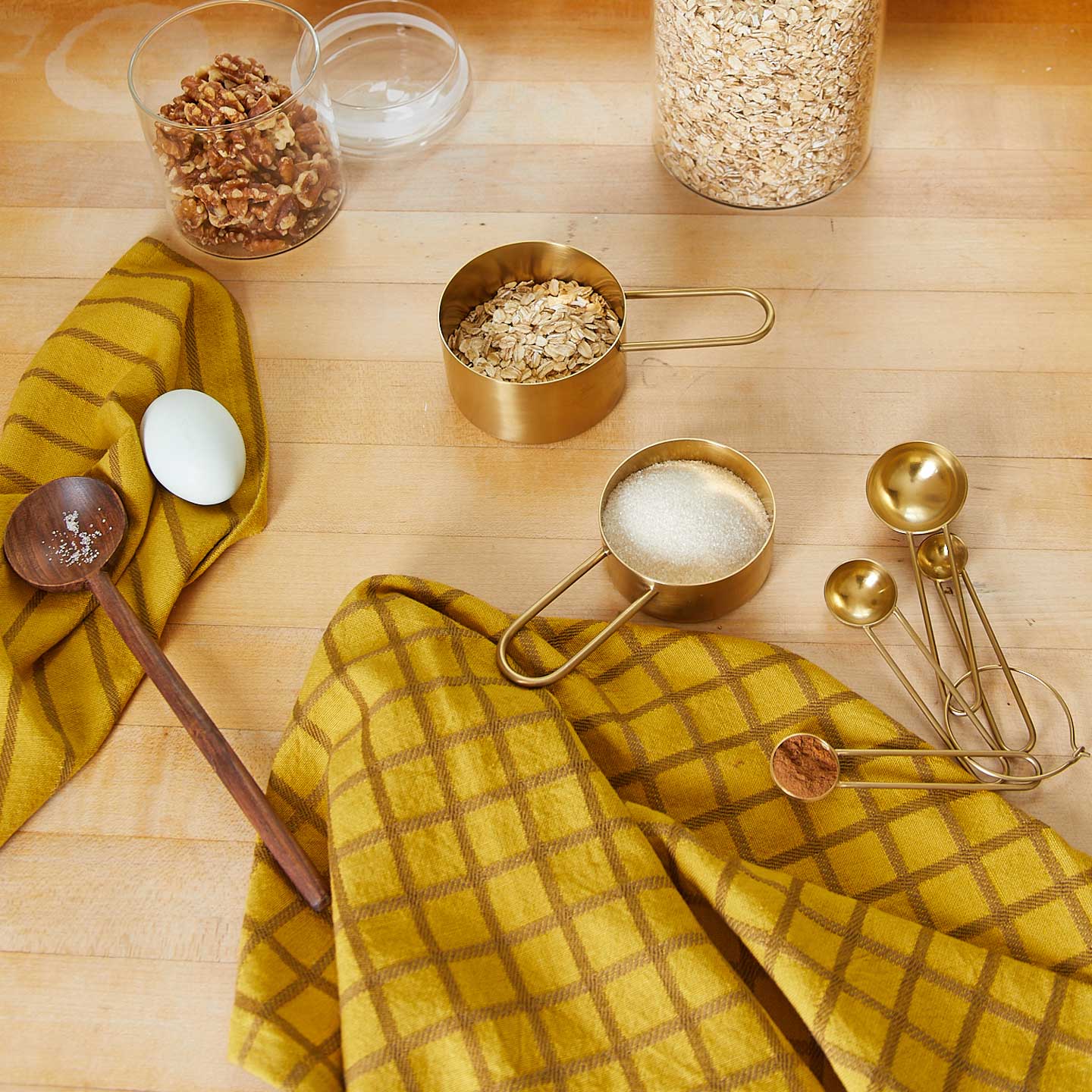Wood countertop with oats, nuts, Simple Measuring Cups and Spoons in Brass, and Essential Yarn Dyed Dishtowels in Mustard.