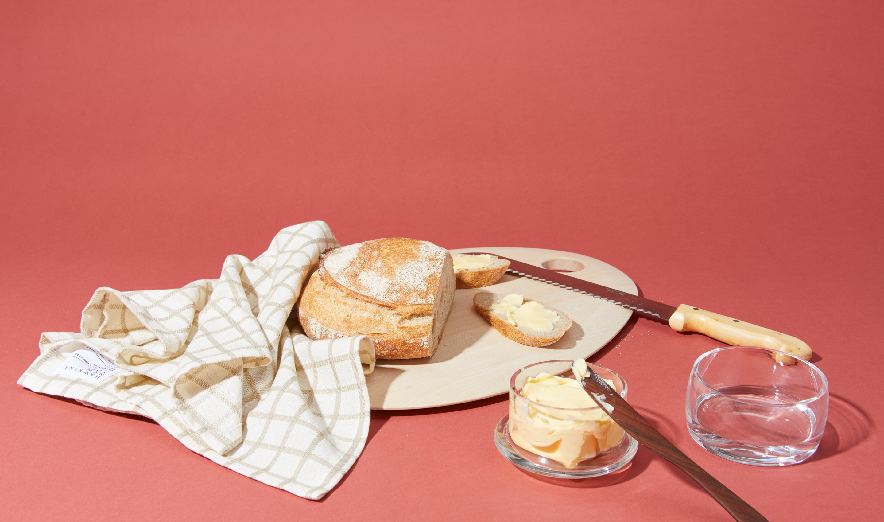 sourdough bread on cutting board with bread knife, dishtowel, butter keeper, and butter spreader