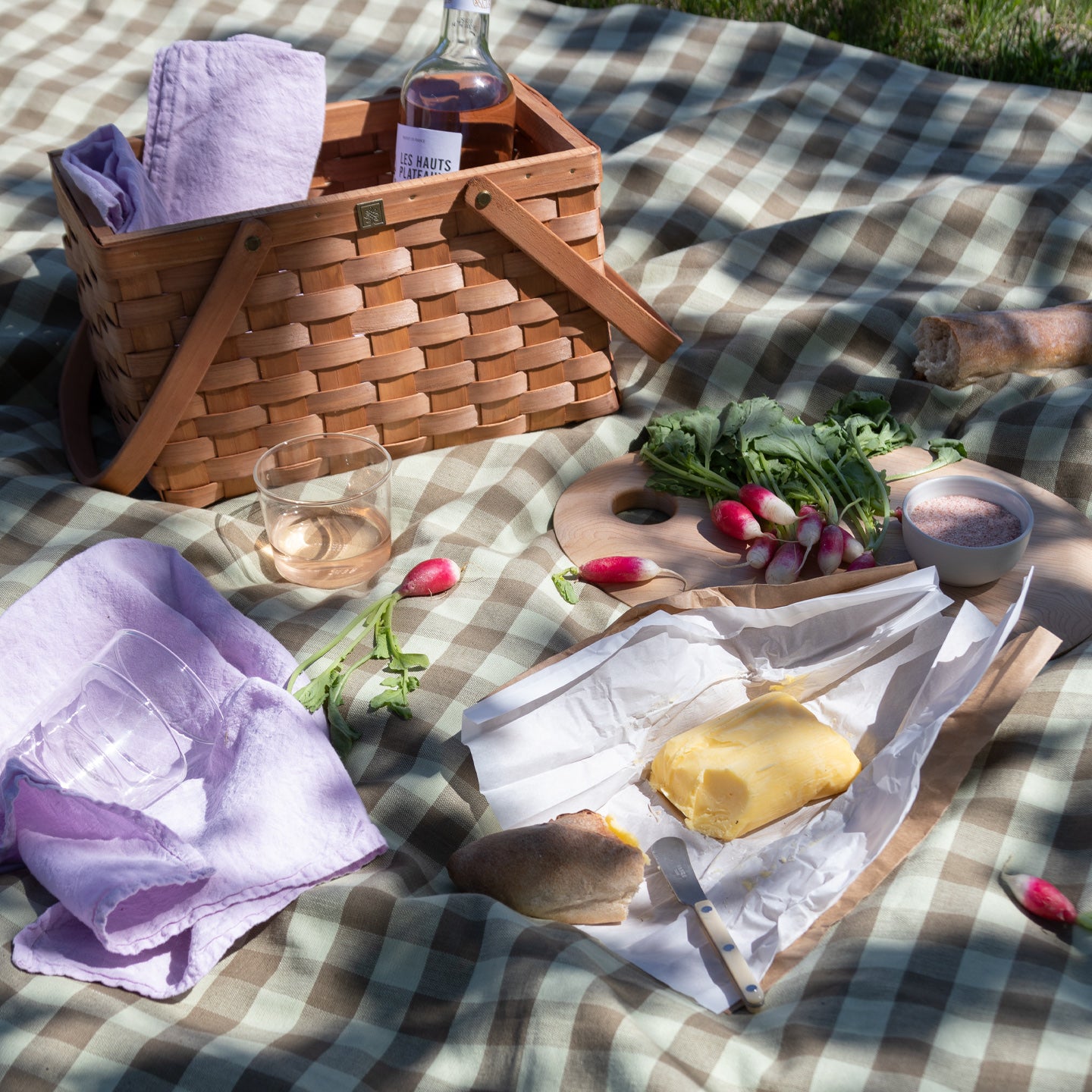Picnic on Essential gingham tablecloth in olive with basket, wine, baguette, butter, turnips, and Essential Glass in clear.