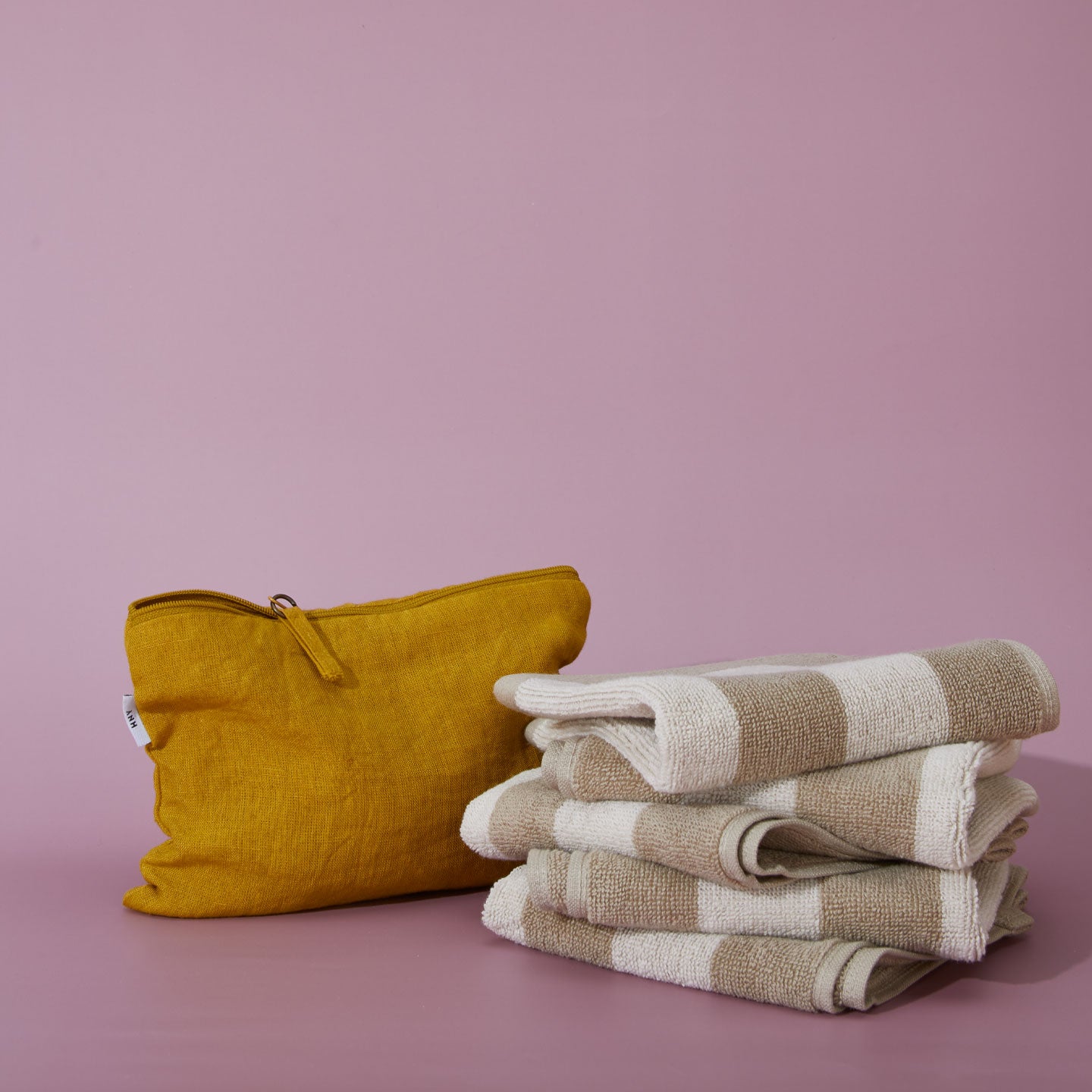 Mustard yellow pouch and stack of folded towels on a lilac background