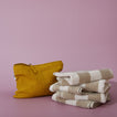 Mustard yellow pouch and stack of folded towels on a lilac background