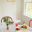 Dining table set with plates of food, a glass of pink drink, and flowers in a room with a window.