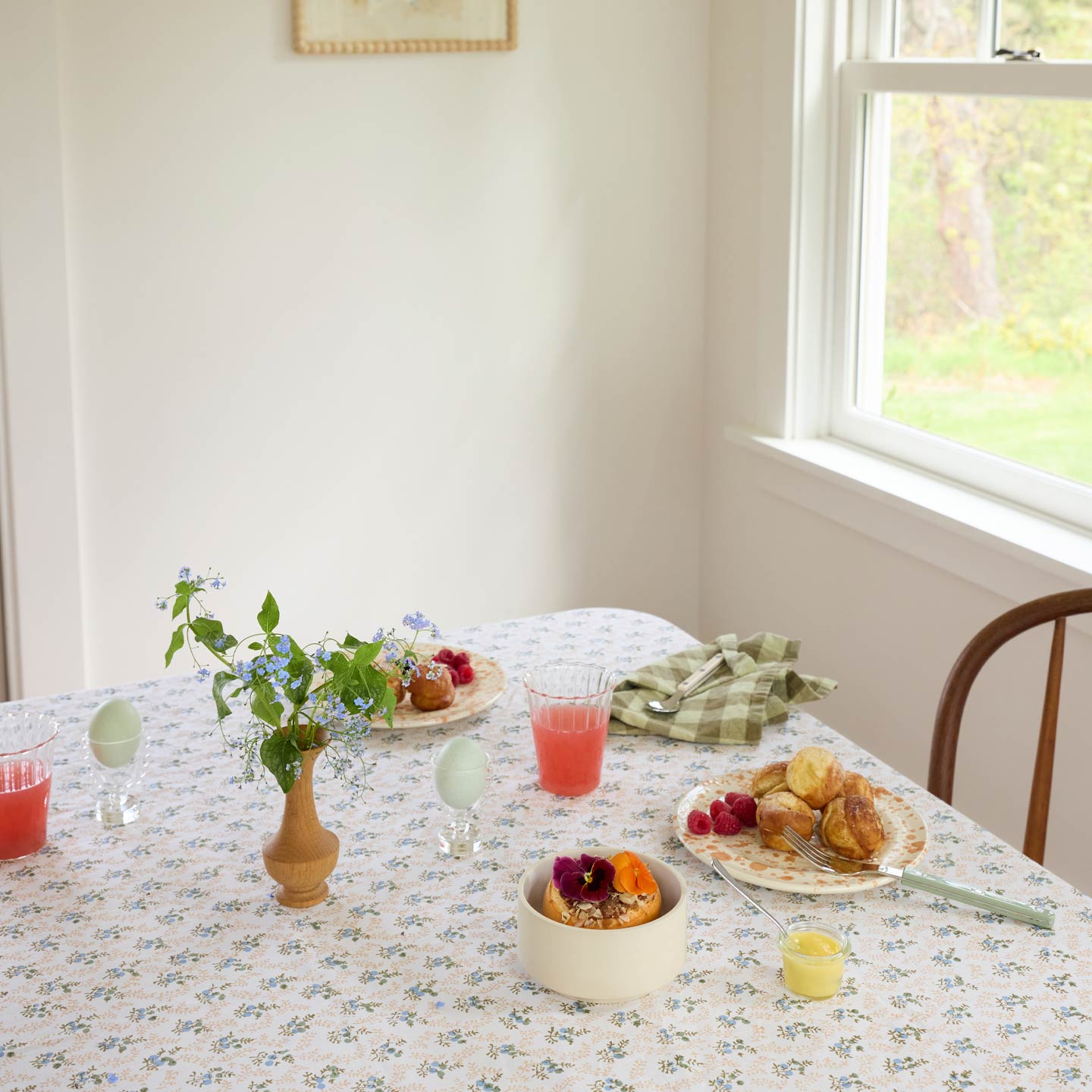 Dining table set with food and drinks in a bright room with a window.