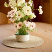 Bouquet of flowers in a white vase on a wooden table with a woven placemat
