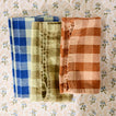 Essential Gingham napkins napkins in olive, blue, and terracotta on a floral tablecloth.