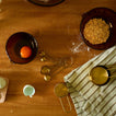 Wooden table with baking ingredients and utensils including a bowl with an egg, a plate with crushed cookies, and measuring cups.