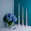 A pair of glass sphere vases filled with flowers and a trio of taper candle holders with taper candles. All in Sky tones.