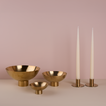A trio of footed bowls and pair of candle holders, all in Brass, with white taper candles.