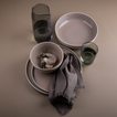 Essential dinnerware, glassware, pitcher, and napkins in Grey tones.