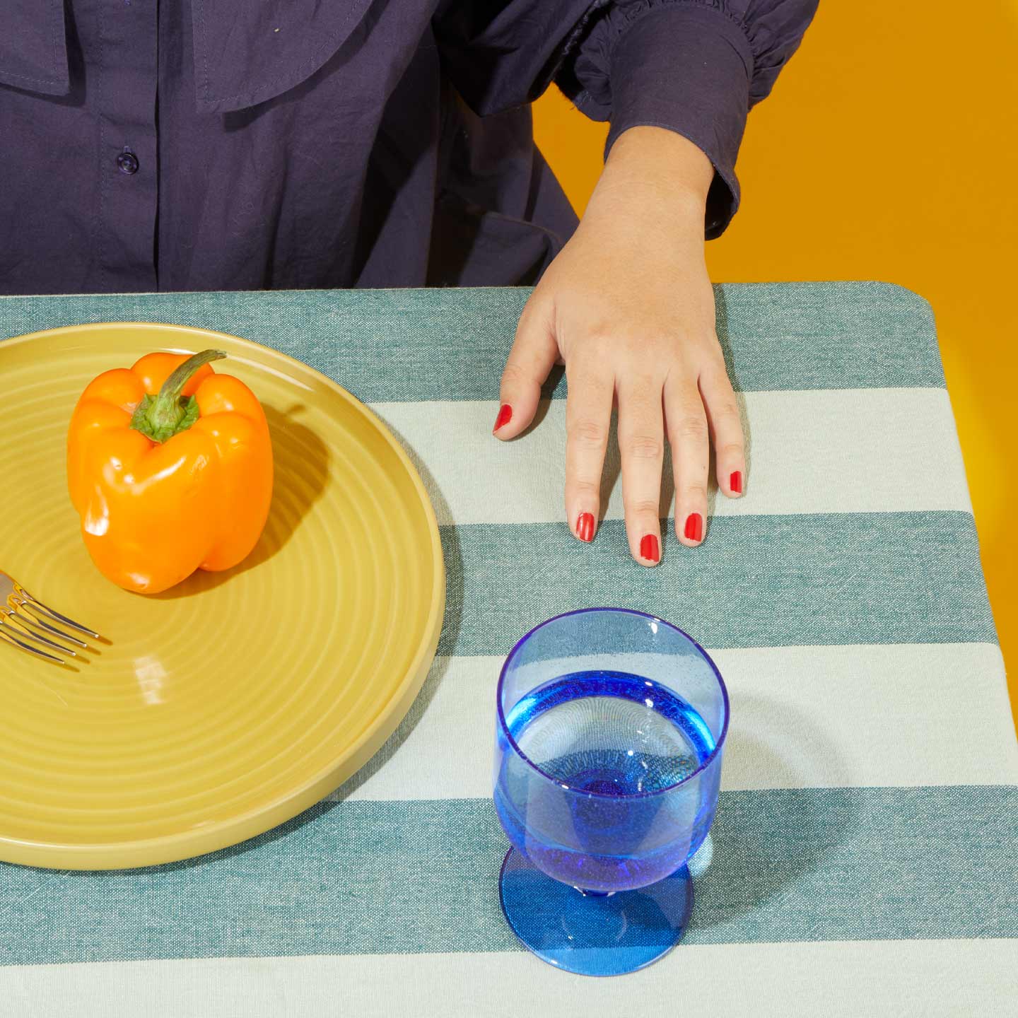 Person sitting at table with Mustard plate with pepper and Blue Simple Seeded Glass with water.