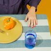 Person sitting at table with Mustard plate with pepper and Blue Simple Seeded Glass with water.