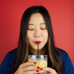 Woman drinking a lemonade with a glass straw against a red background