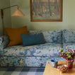 Den with floral sofa, art, wall lamp, and coffee table with mug, nuts, and vase.