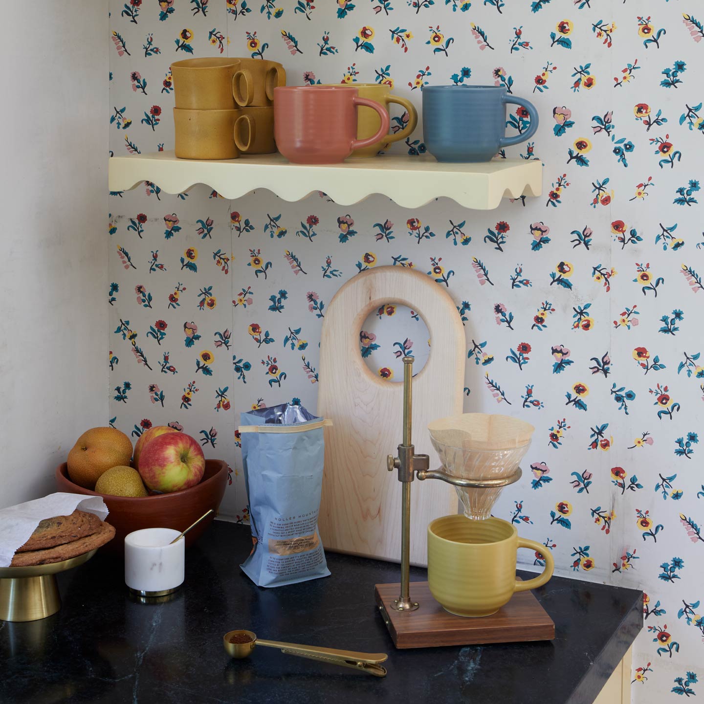 Coffee brewing setup with a yellow mug, floral wallpaper, and various kitchen items on a shelf.