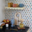 Coffee brewing setup with a yellow mug, floral wallpaper, and various kitchen items on a shelf.