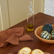 Wooden table with a bowl of squashes, a bottle of oil, and terracotta dish towel.