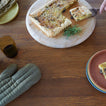 Wooden cutting board with a square pizza and a glass of dark liquid on a wooden table.