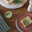 Square of savory tart on a pink plate with a wooden table setting