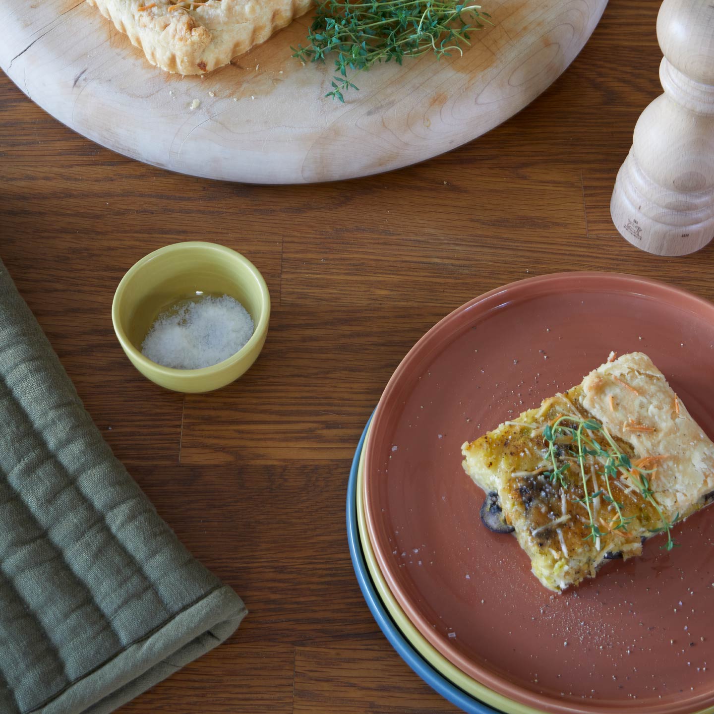 Plated dish with a piece of tart on a wooden table, accompanied by a small bowl and salt shaker.