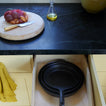 Top view of a kitchen counter with a cutting board, knife, and oil bottle, and a bottom view of a drawer with a cast iron skillet.