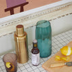 Party bar with shaker, glass with lemon peel, cutting board with knife, and Essential Glass Pitcher in Peacock with ice.