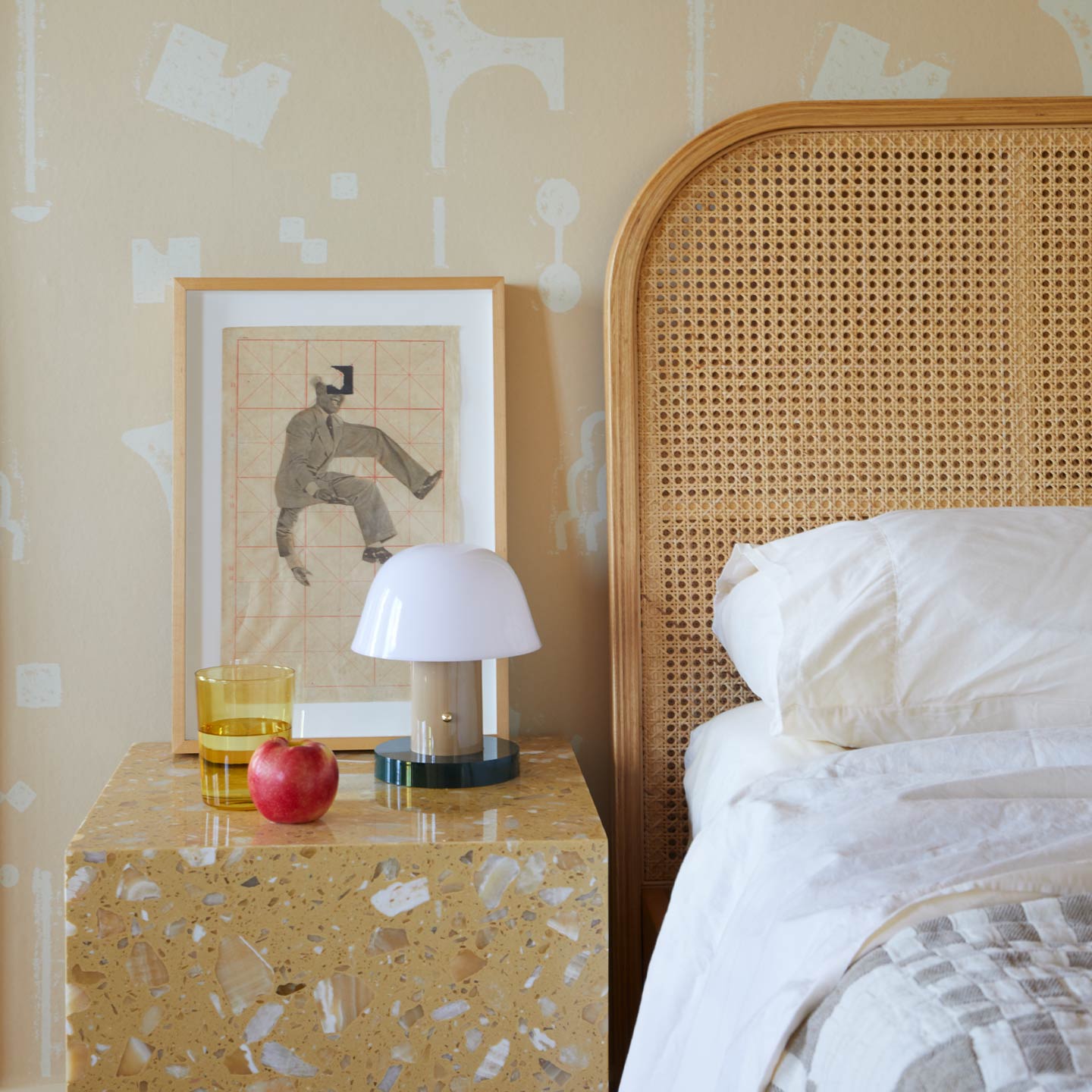 Bedroom with wicker headboard, nightstand with lamp and glass, and abstract wall art.