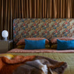 Bed with patterned headboard and bedding in terracotta, peacock, bronze, and multicolor throw.
