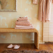 Stack of pink towels on a woven bench against a wall with decorative wallpaper.