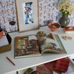 Open book on a table with decorative items including a vase, glass, and framed art.