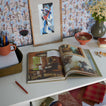 Open book on a table with decorative items including a vase, bowl, and framed picture.