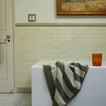 Bath scene with Olive Striped Towel on bathtub and Essential Glass in Terracotta.