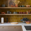 Kitchen with wooden shelves displaying ceramic items against a green tiled wall.