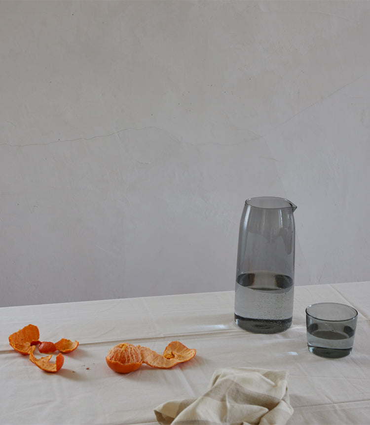 A glass pitcher and a partially filled glass sit on a white tablecloth next to scattered orange peels.