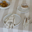 Place setting with Essential Dinnerware and Essential Striped Napkin in Ivory and Essential Striped Tablecloth in Ivory with flatware and grapes.