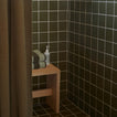 Bathroom corner with dark tiled walls, a wooden shelf with towels and a bottle, and a shower curtain.
