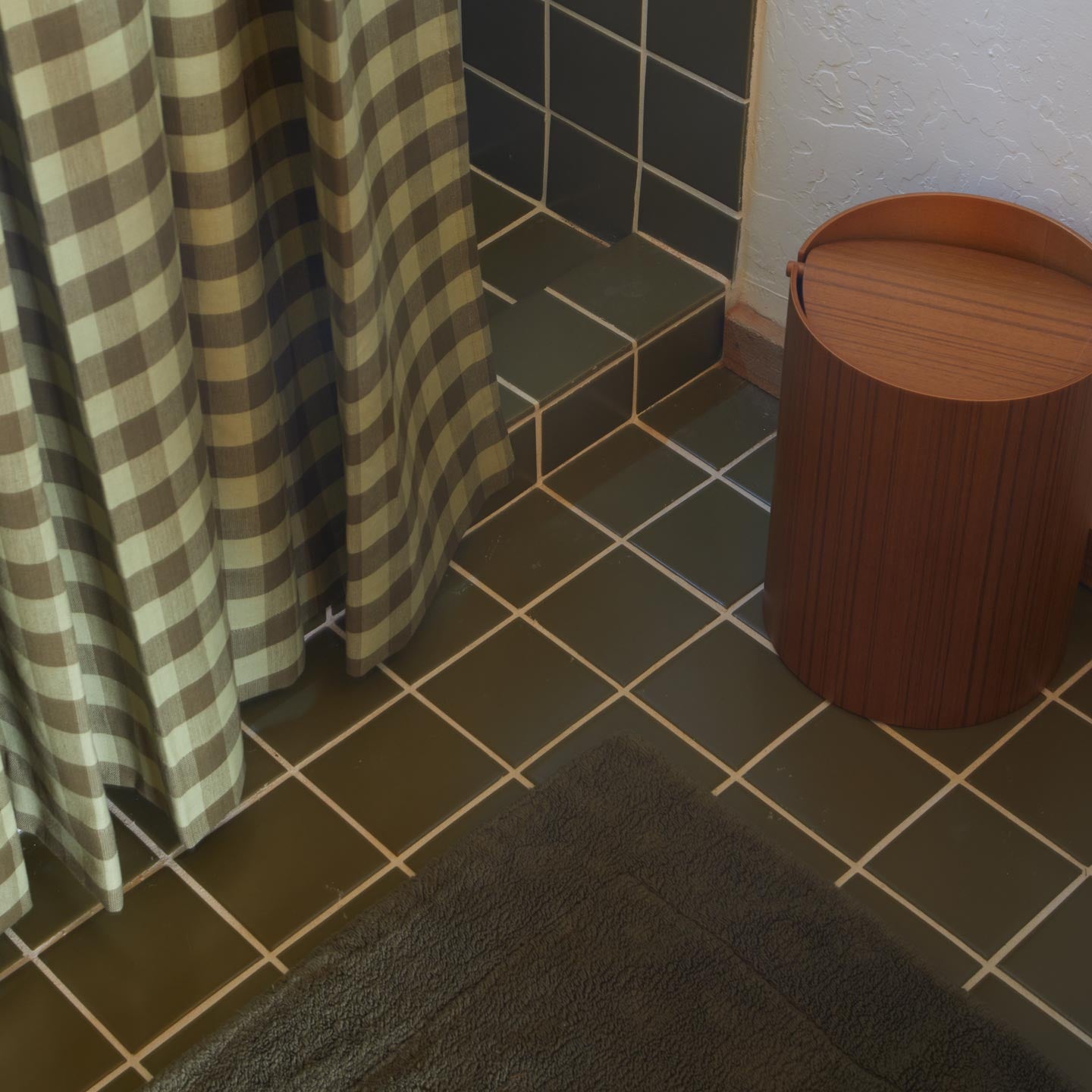 Bathroom with tiled floor, gingham curtain, and wooden trash can.