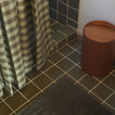 Bathroom with tiled floor, gingham curtain, and wooden trash can.