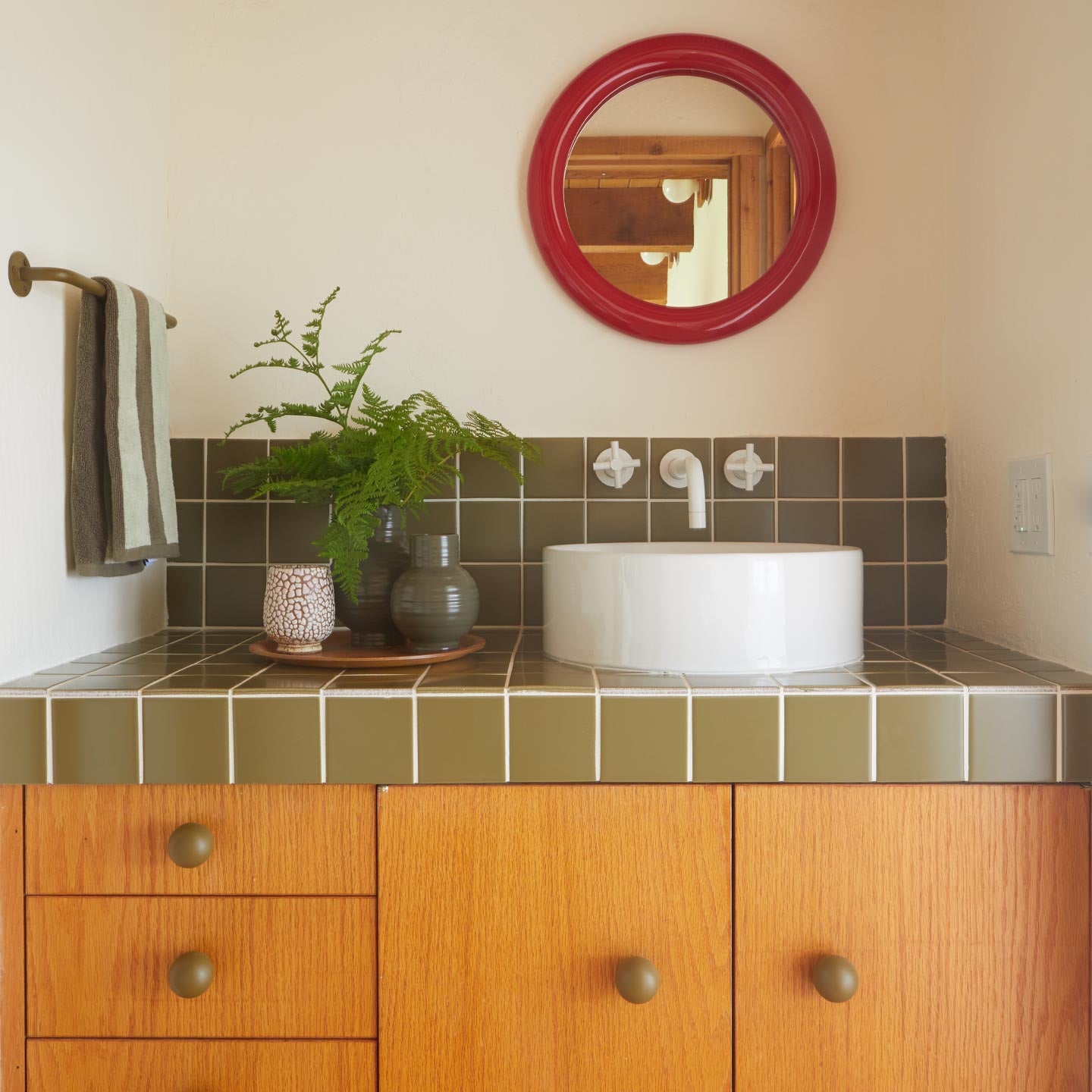 Bathroom with wooden vanity, white sink, and red mirror.