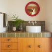Bathroom with wooden vanity, white sink, and red mirror.