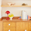 Wooden dresser with a red lamp, white vase with yellow flowers, books, and decorative items.