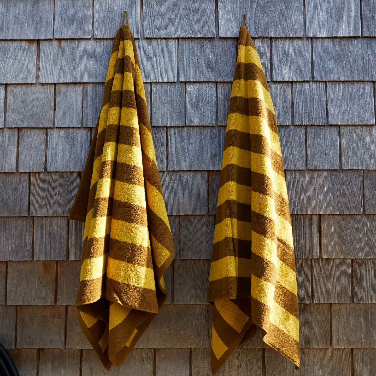 Two mustard and bronze striped towels hanging on a wooden shingled wall.