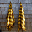 Two mustard and bronze striped towels hanging on a wooden shingled wall.