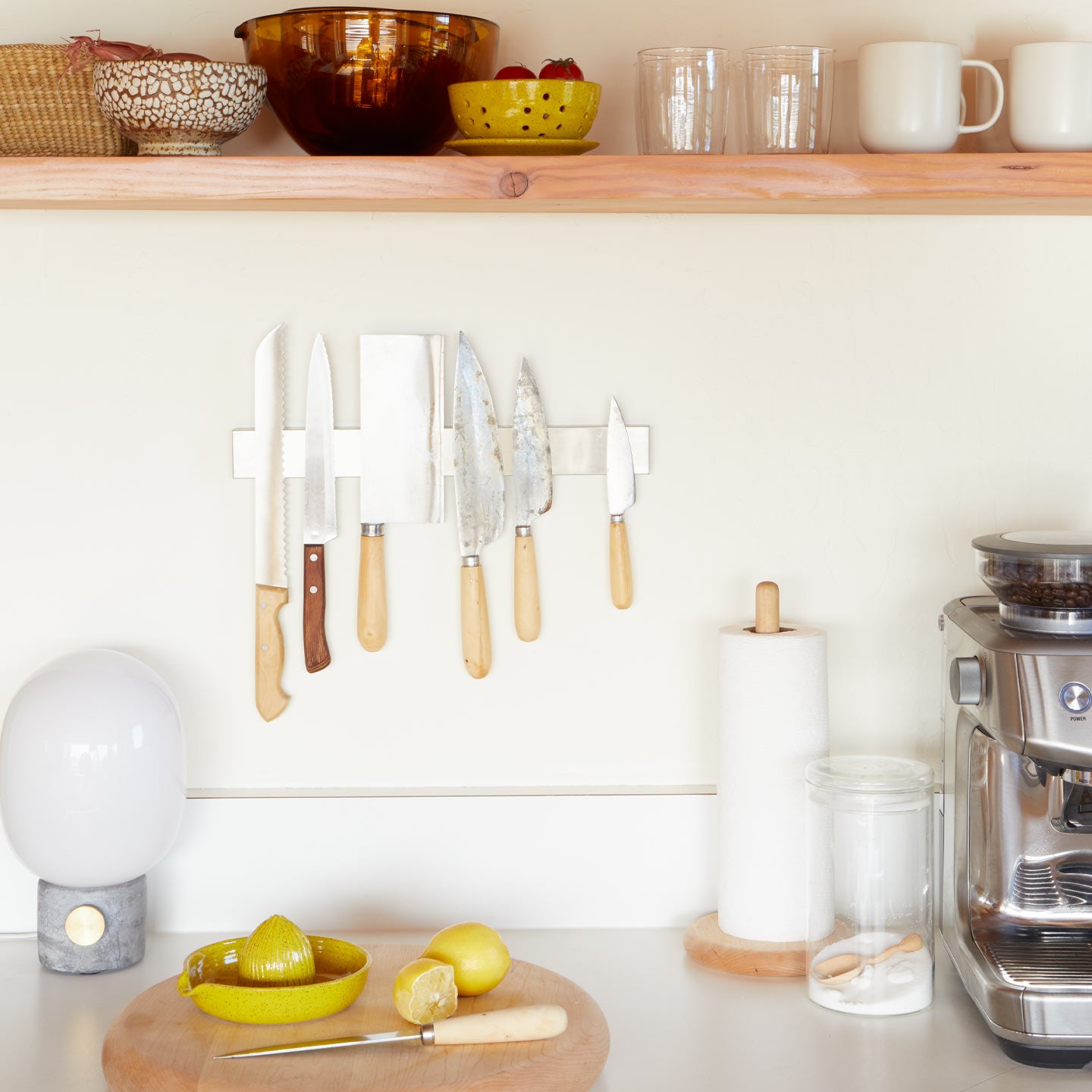 Kitchen counter with knives on a magnetic strip, lemons, a cutting board, and a coffee maker.
