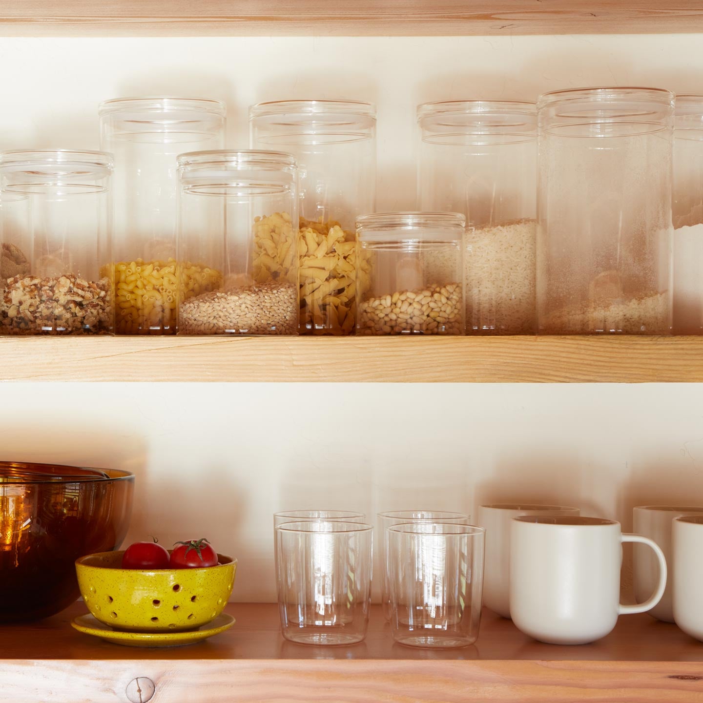 Shelf with glassware, essential glass storage, tomatoes in berry bowl, and simple porcelain mugs.