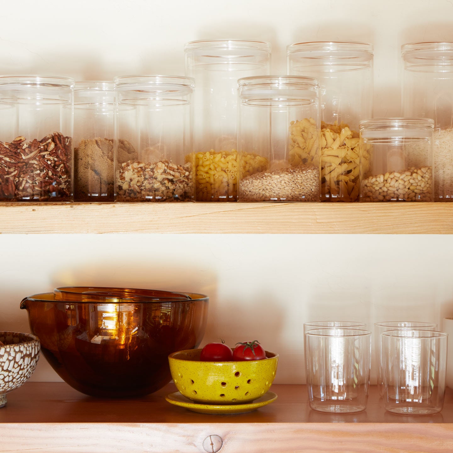 Kitchen shelves with jars of dry goods and a bowl of tomatoes.