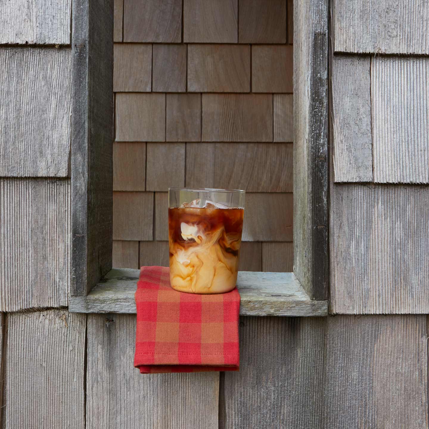 Iced coffee in Clear Essential Glass with Essential Gingham Napkin in window.