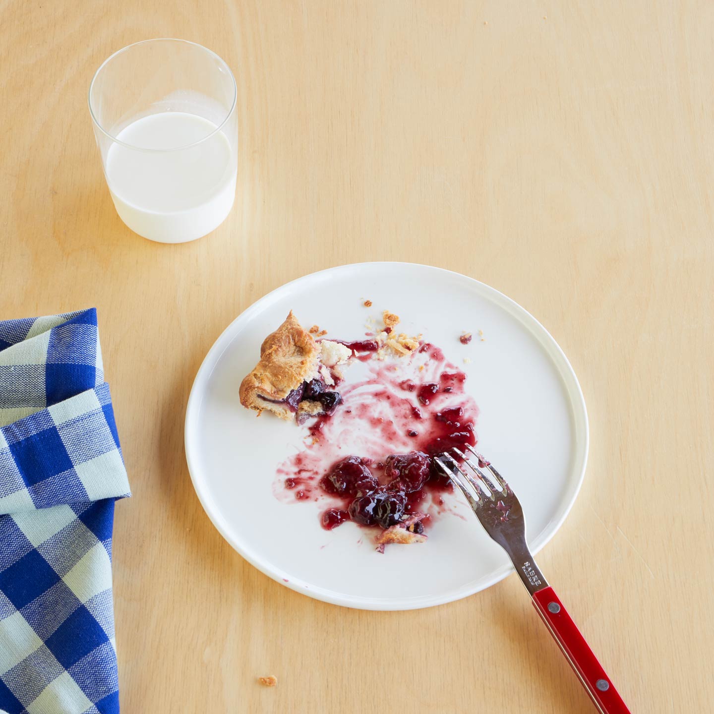 Overhead table setting with Simple Porcelain Salad Plate with pie, Essential Glass with milk, Sabre fork, and Essential Gingham Napkin in Blue.