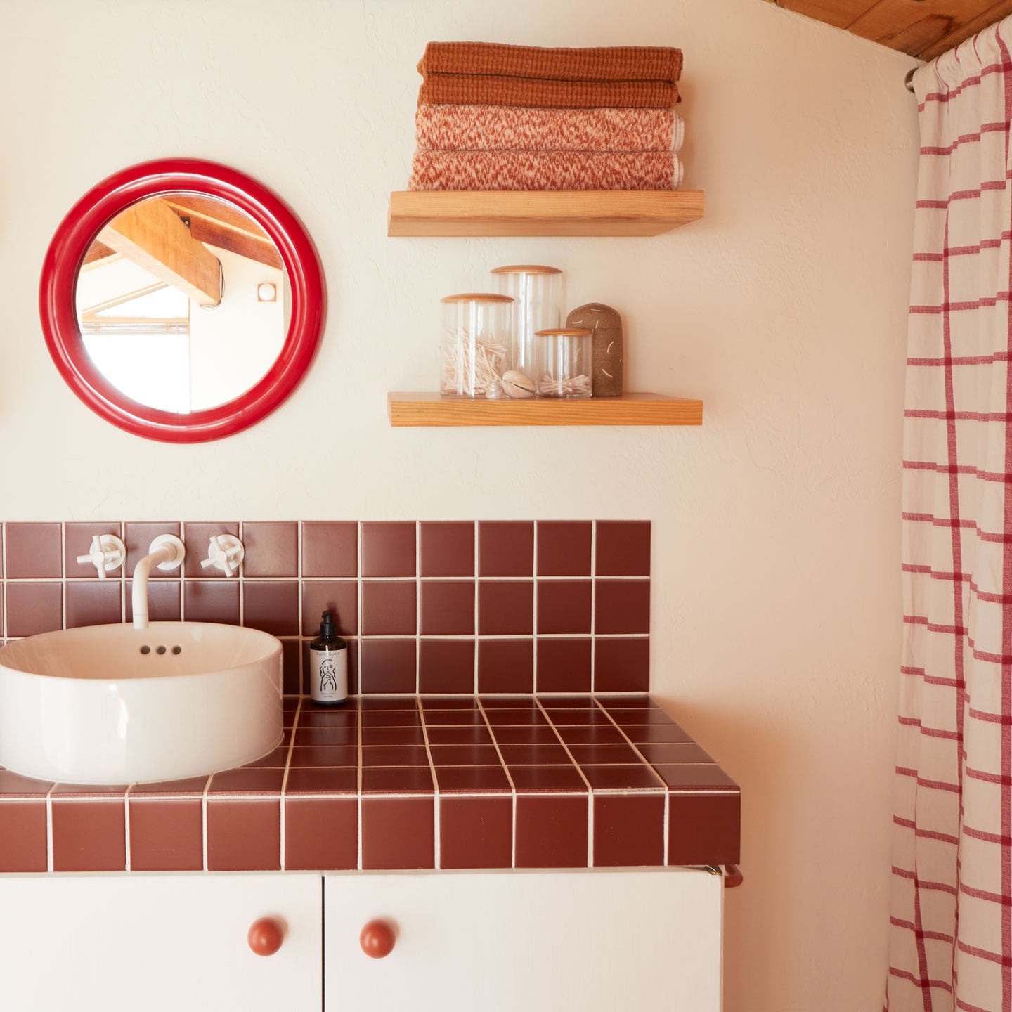 Bathroom with red tiled countertop, white sink, and wooden shelves.