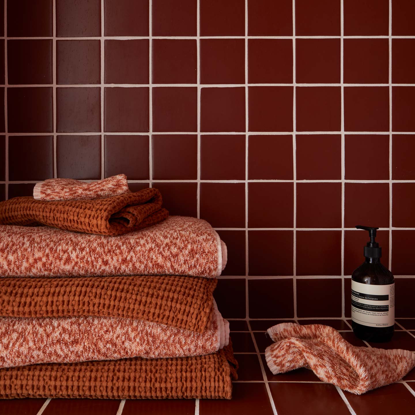 Stack of terracotta towels against a red tiled wall with a bottle of soap.